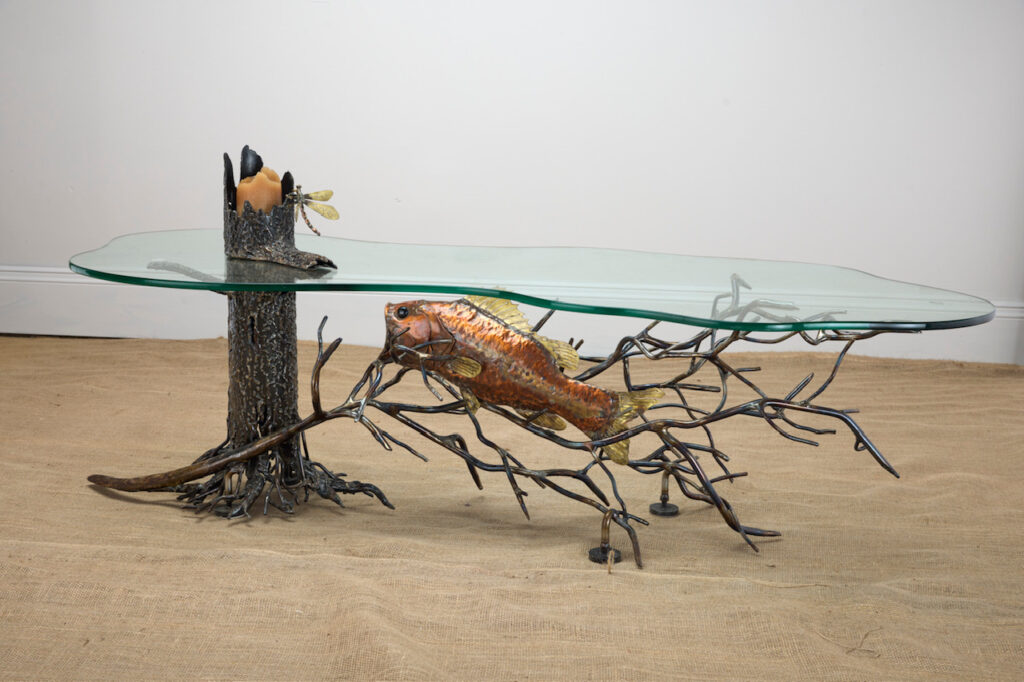 Glass-topped table with a metal fish swimming through welded branches