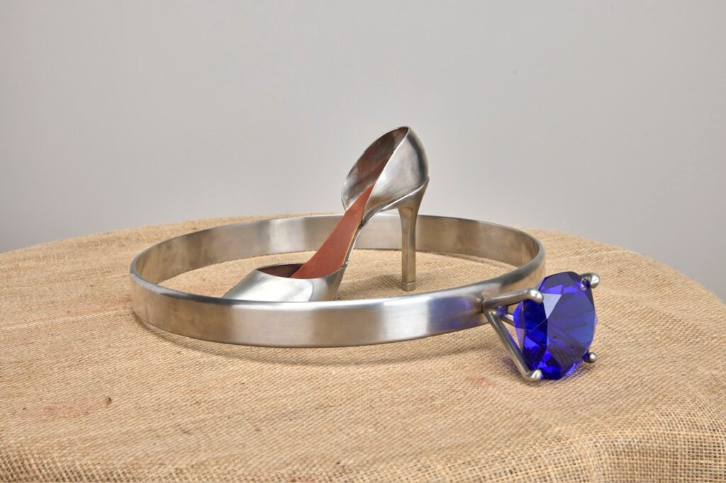 Stainless high-heel shoe beside an oversized ring with a blue stone