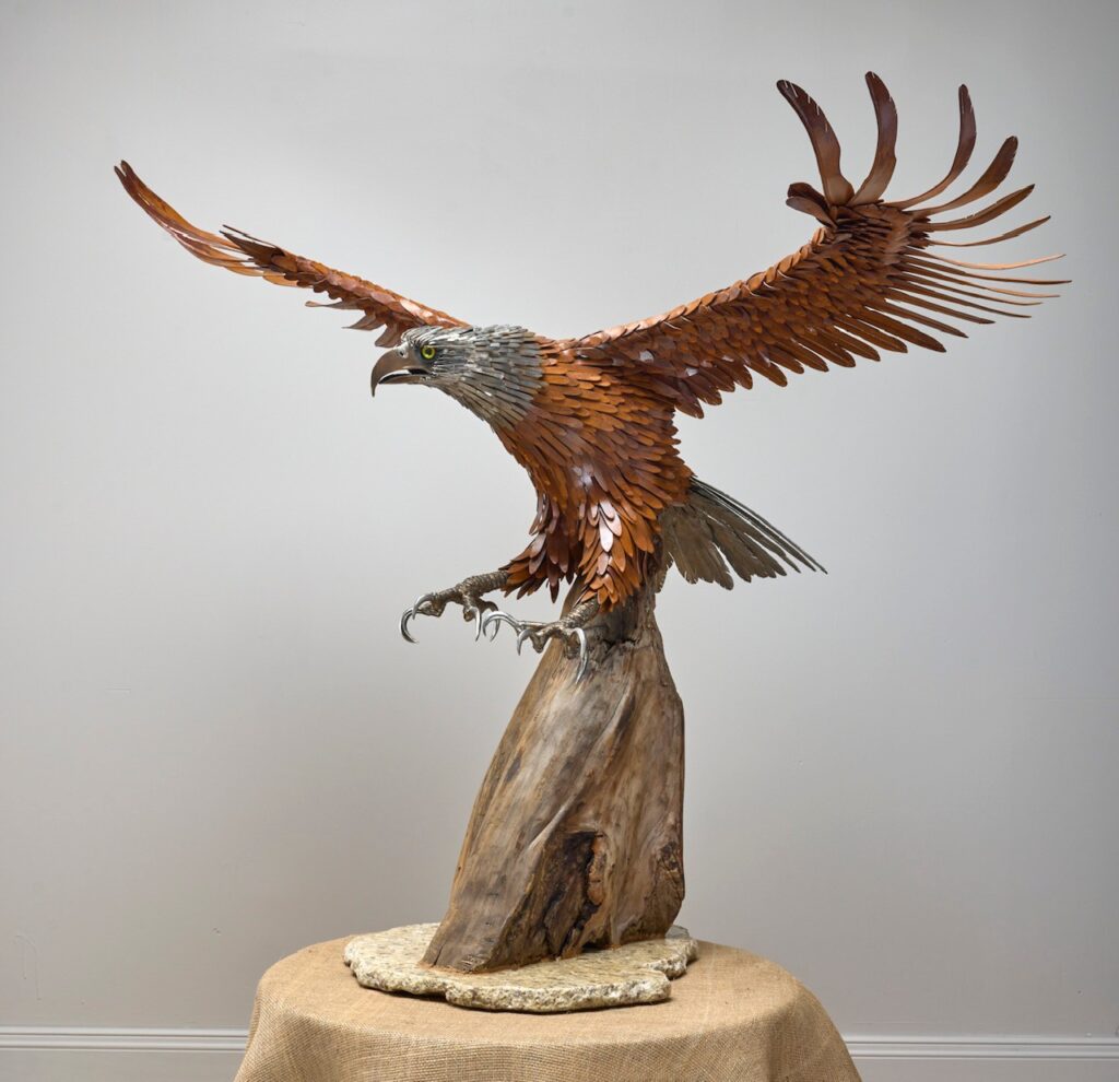 Hand-hammered metal eagle with outstretched wings landing on driftwood