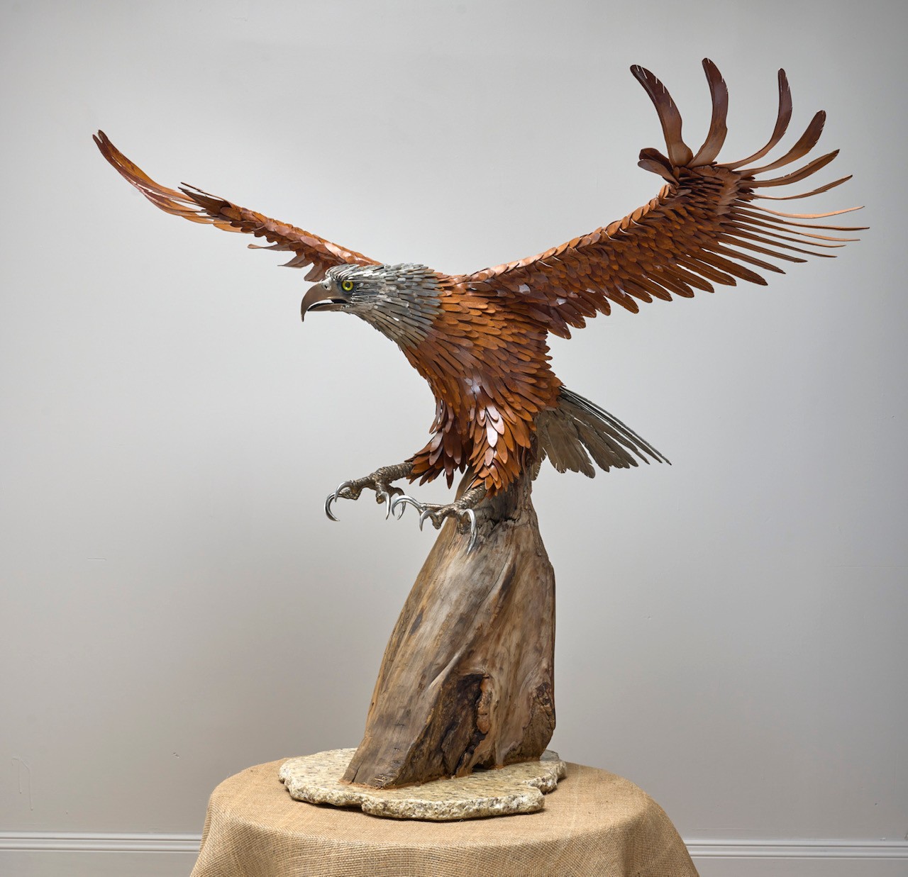 Hand-hammered metal eagle with outstretched wings landing on driftwood
